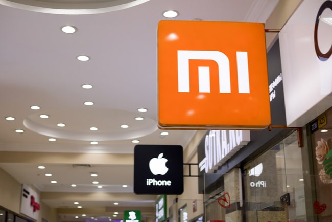Skylt med Apples logotyp bakom skylt med Xiaomis logotyp i köpcentrum.