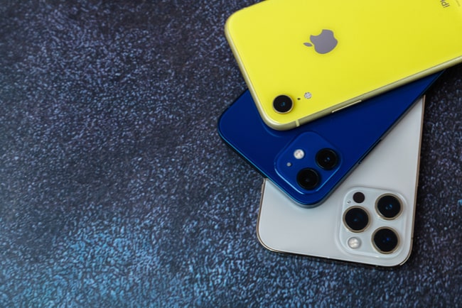 Tre stycken Iphones ligger staplade på varandra; en vit, en mörkblå och en gul.